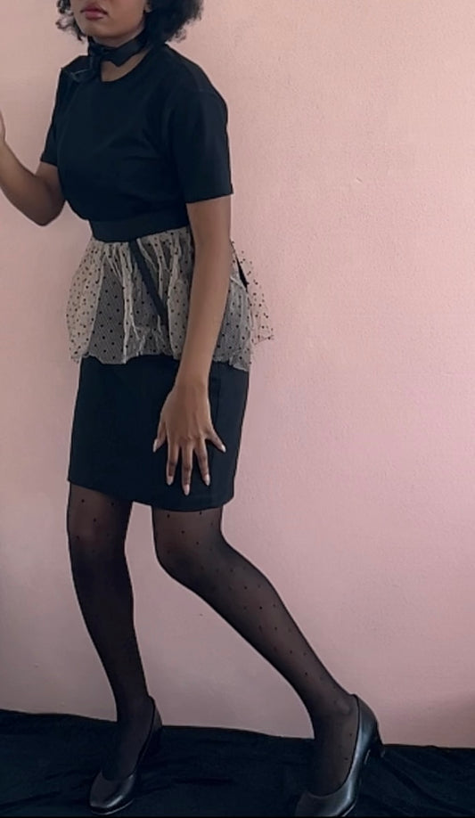 A model wearing KimYoung's knee-length black pencil skirt with a pink peplum peplum and black polka dots with KimYoung's signature black ribbon chain with a black bow with pearl on it, paired with a black top and black heels. 