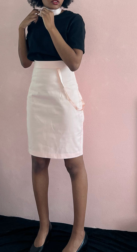 A model wearing KimYoung's knee-length pink pencil skirt with KimYoung's signature  ribbon chain in pink, paired with a black top and black heels. 